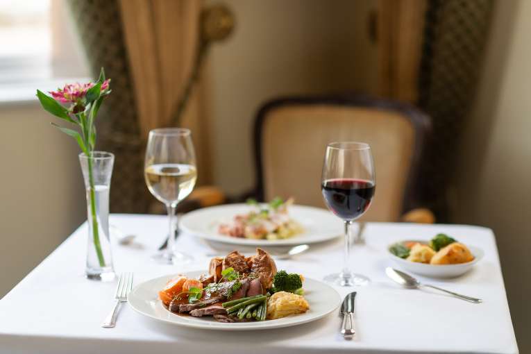 2 plates of food with a glass of red and white wine on a table in The Belmont Restaurant