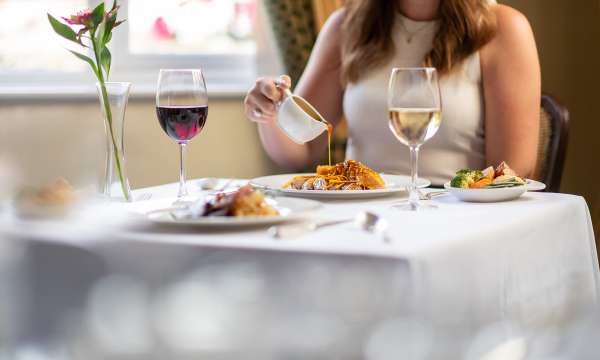 Someone pouring sauce over duck dish sat at a table in The Belmont Restaurant