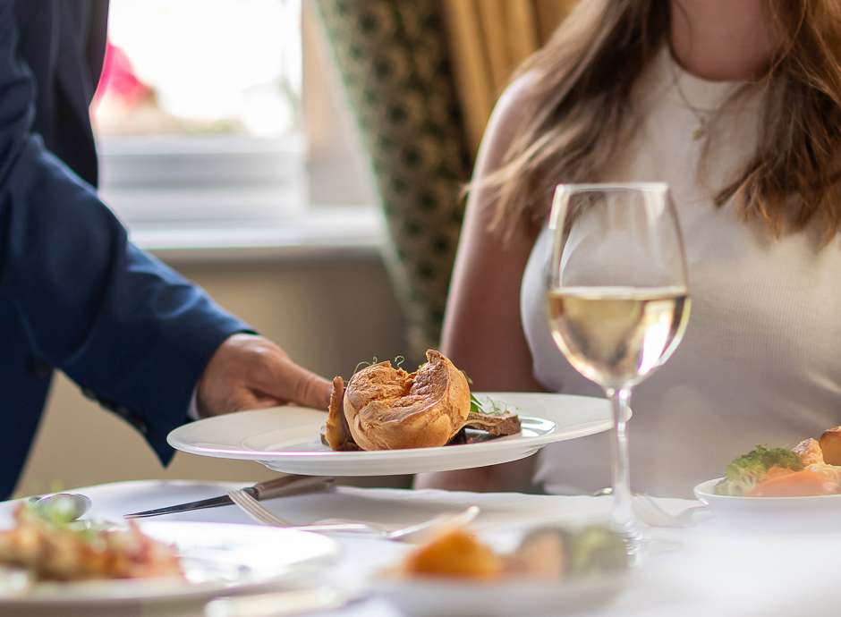 A waiter's hand putting down a Sunday Roast for a women sat at a table
